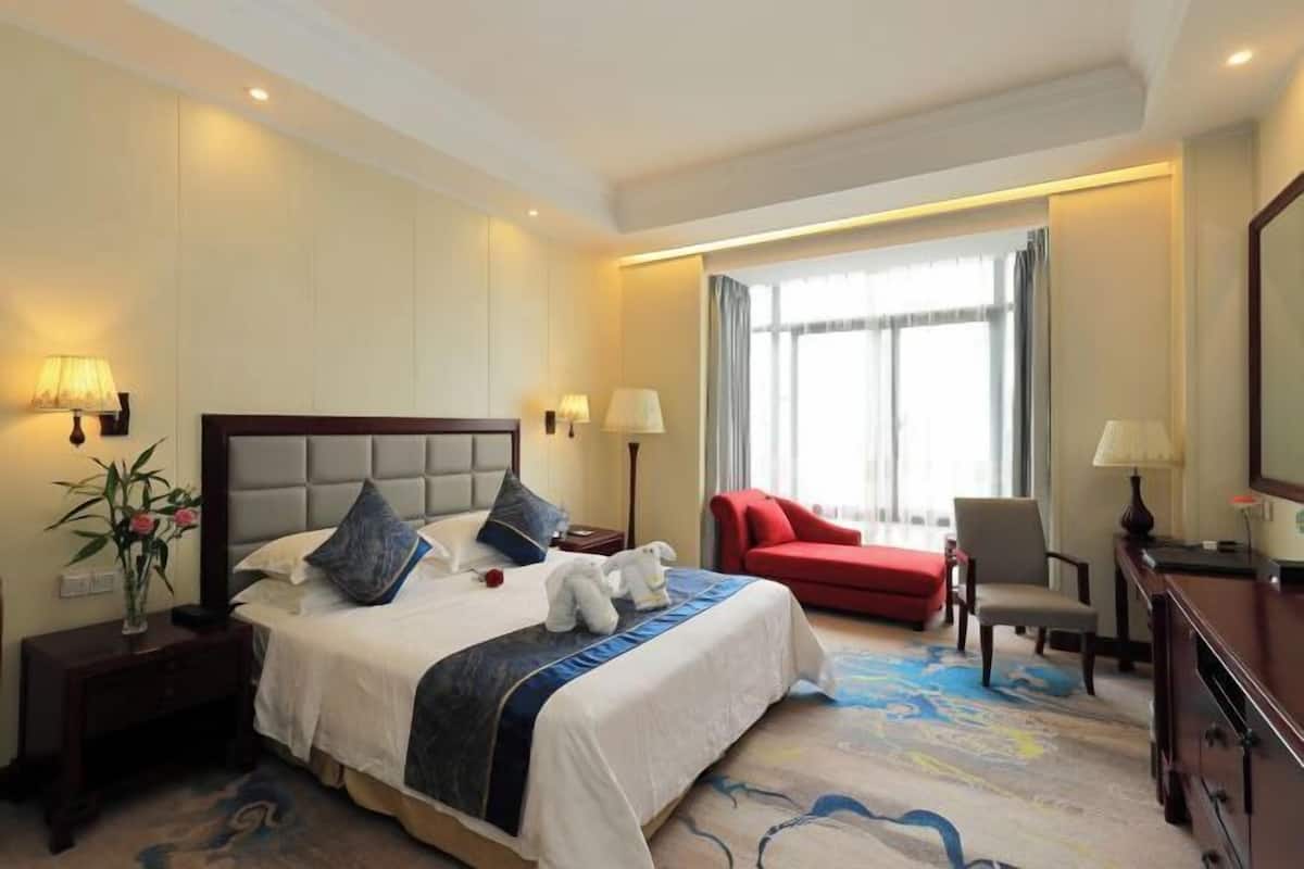 A hotel room with a large bed, bedside tables, a desk, a chair, and a window with curtains.