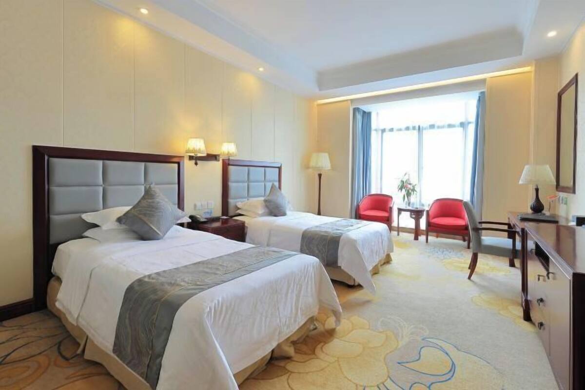 A hotel room with two beds, a desk, a chair, and a window with curtains.