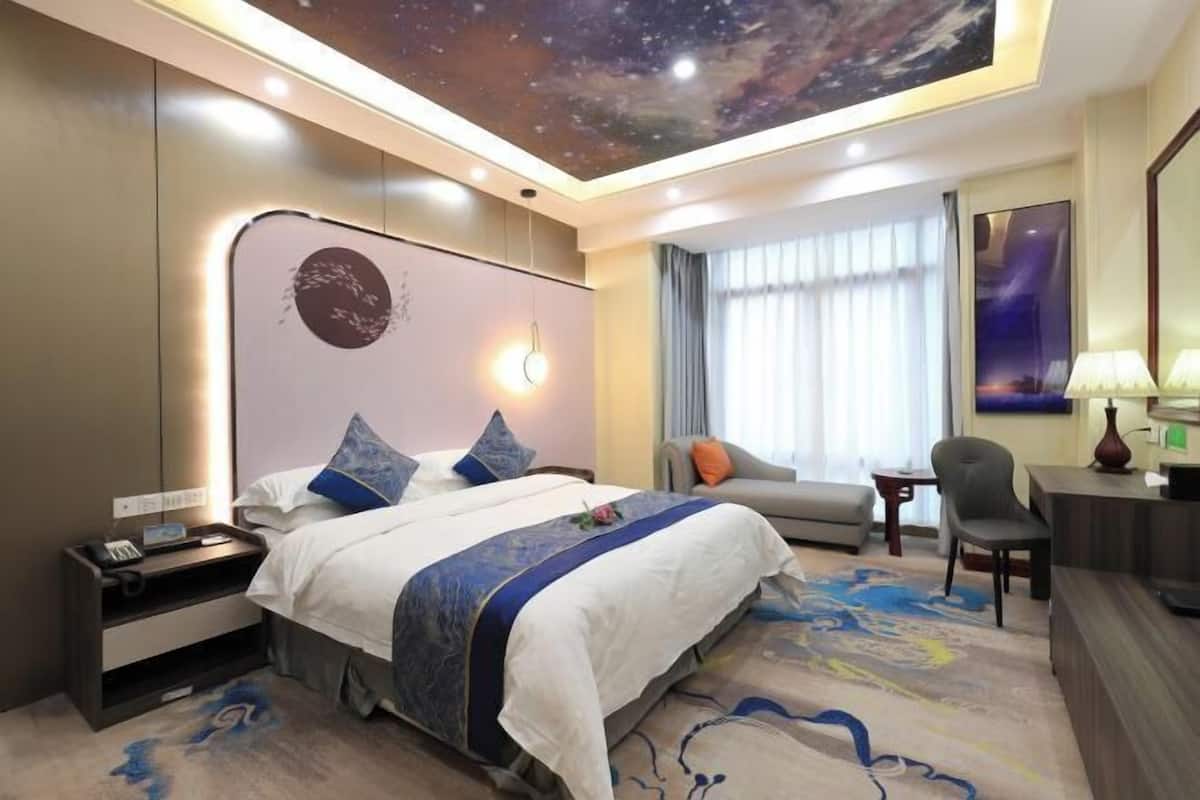 A hotel room with a bed, a sofa, a desk, and a desk lamp.