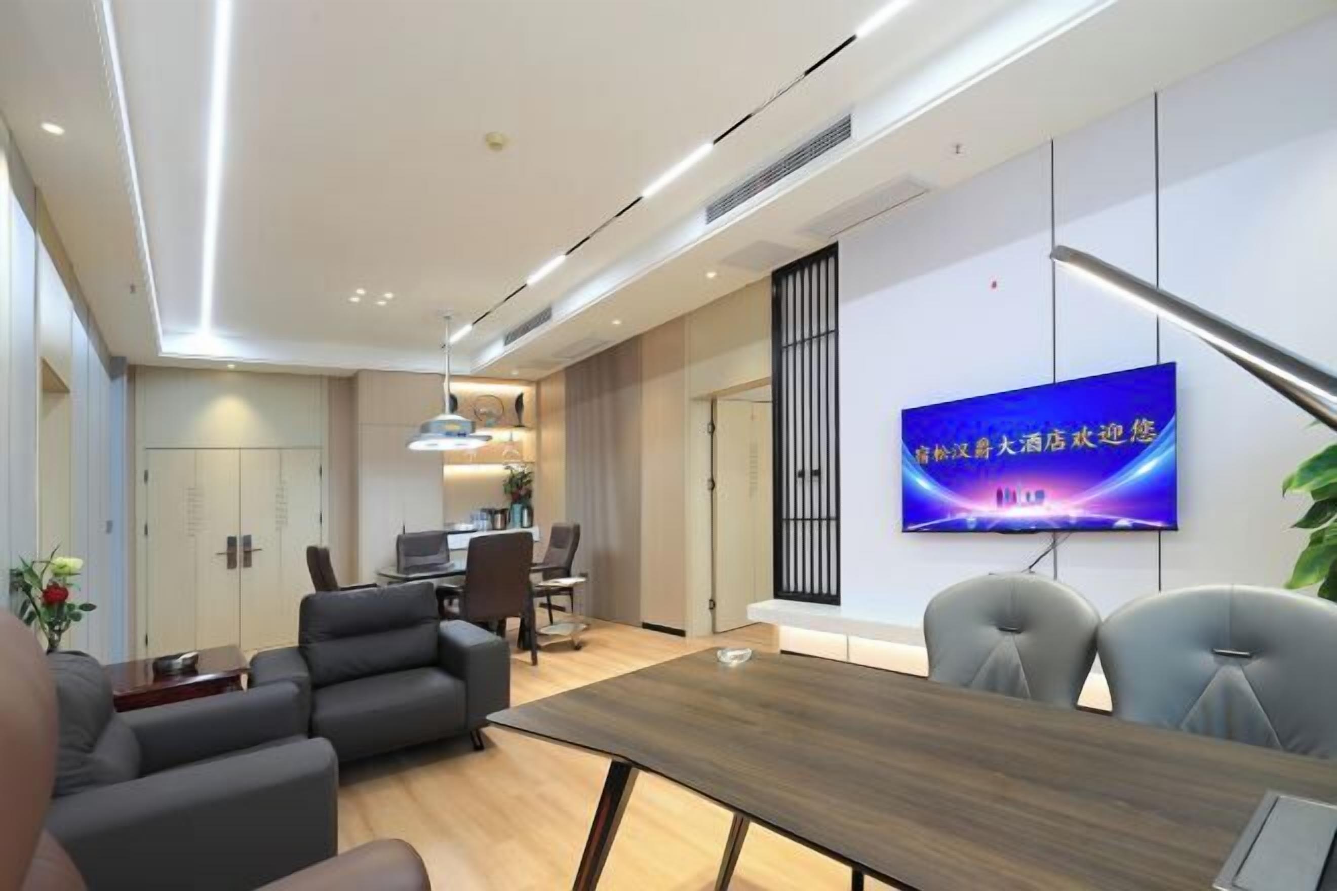 A modern conference room with a wooden table, grey chairs, and a large TV on the wall.