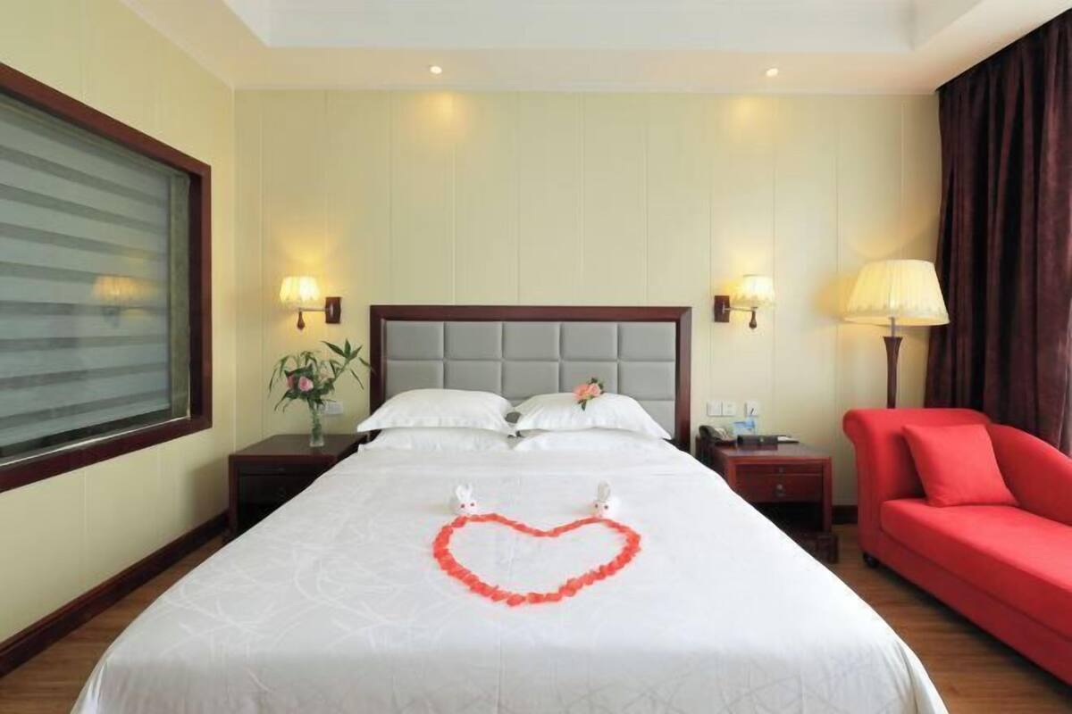 A hotel room with a large bed, a red sofa, and a heart-shaped decoration on the bed.