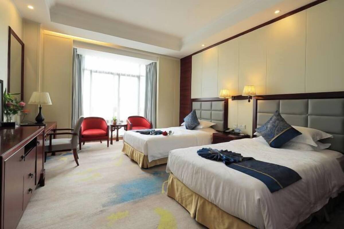A hotel room with two beds, a desk, a chair, and a window with curtains.