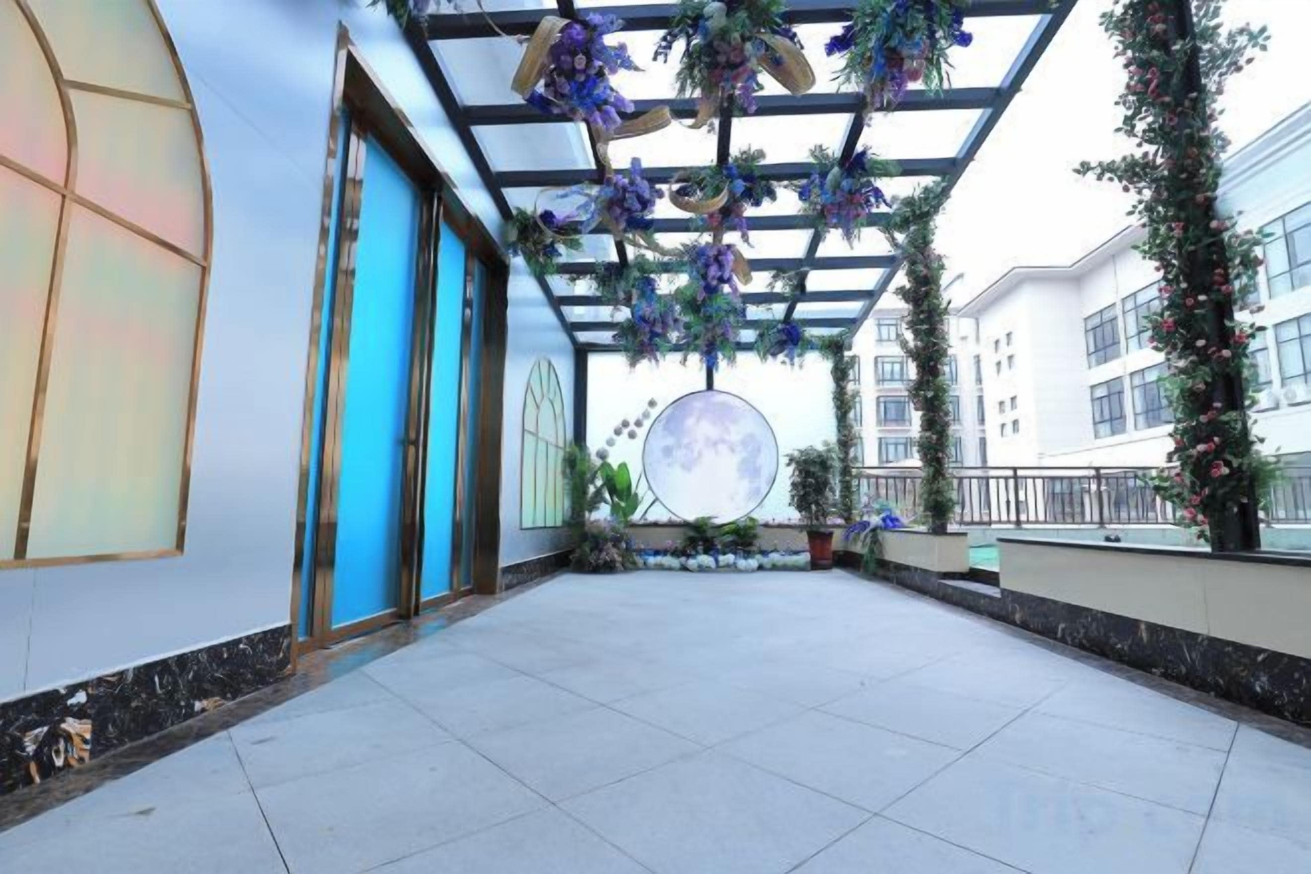 Un espacio al aire libre cubierto con piso de baldosas, un ventanal circular grande y decoraciones florales colgantes.