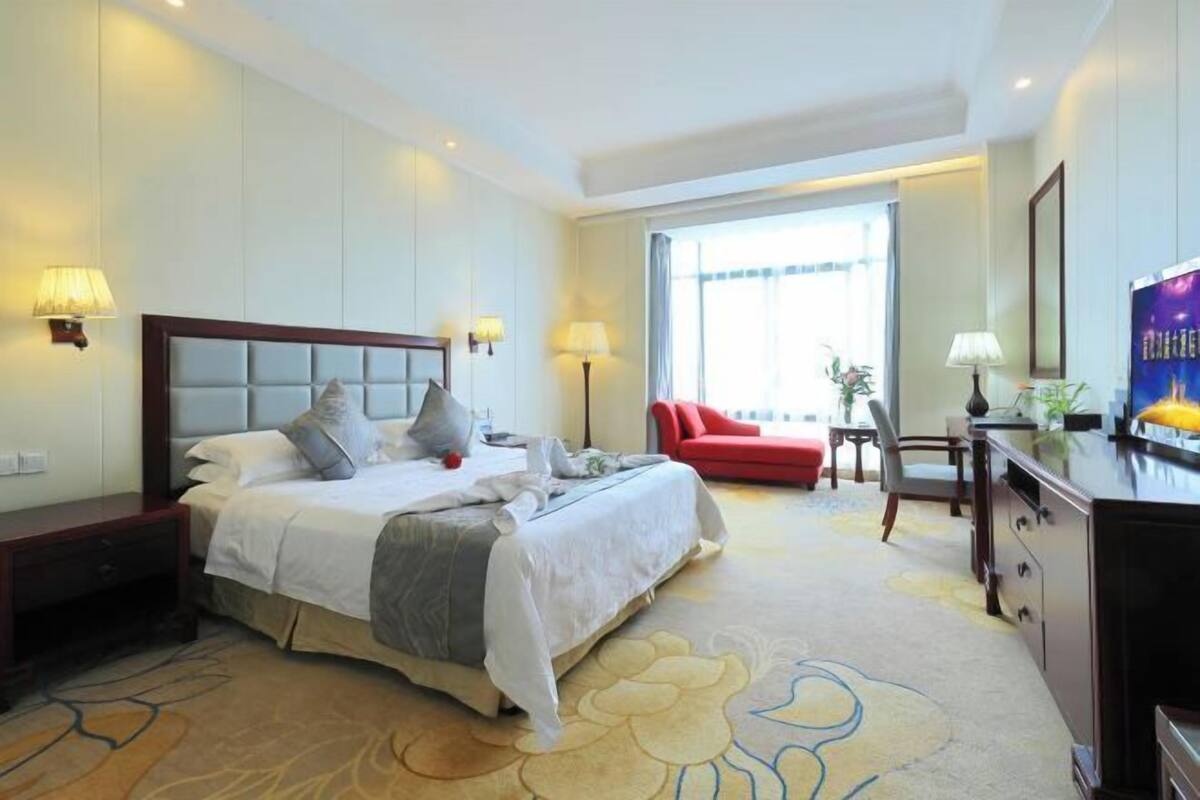 A hotel room with a bed, bedside tables, a desk, a chair, a red sofa, and a television.