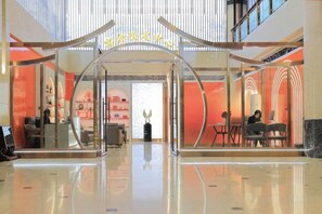 Vestíbulo de hotel con entrada de cristal, zona de estar y mostrador de recepción.