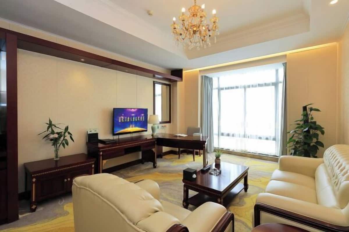A hotel room with a television, sofa, coffee table, and a large window.