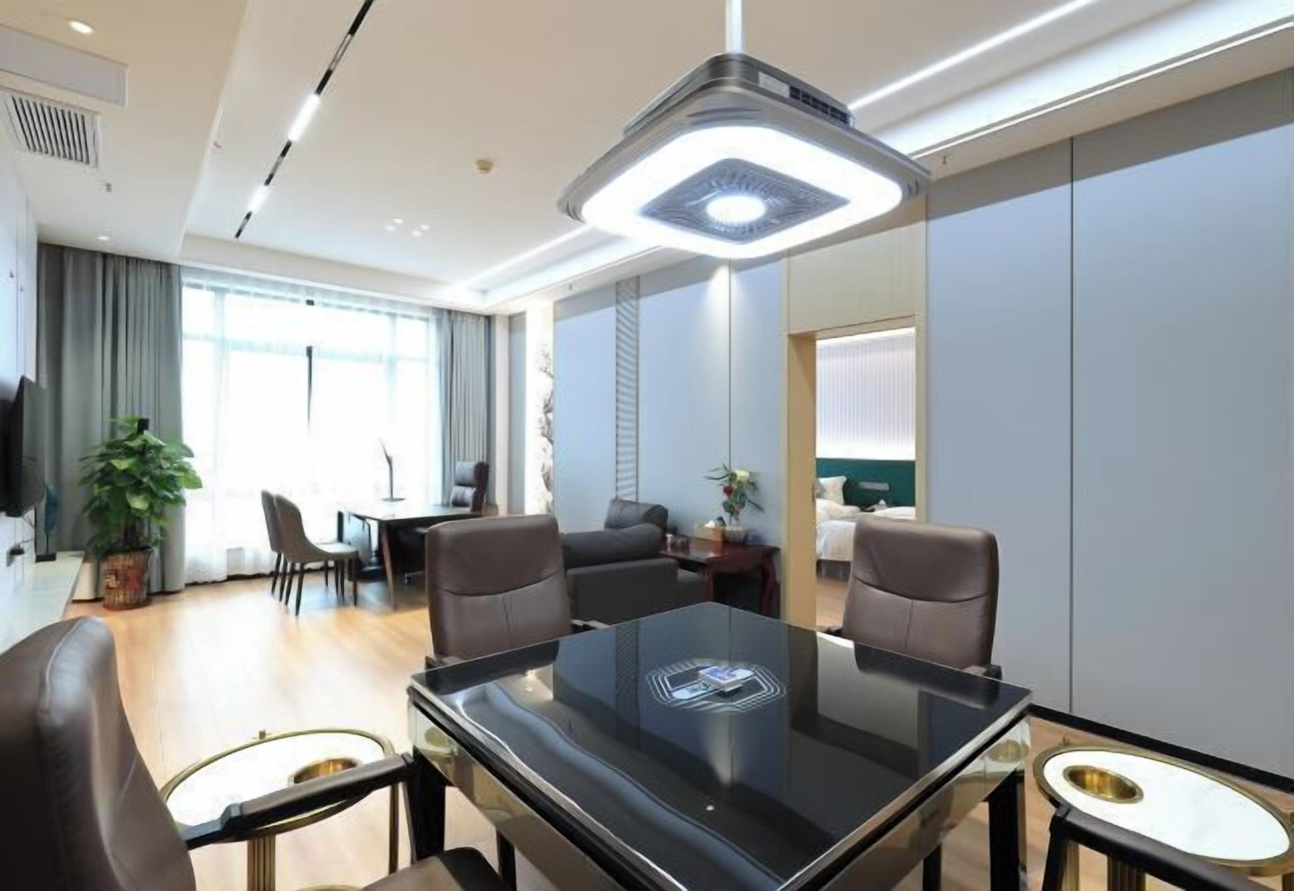 Habitación de hotel moderna con una mesa de comedor de cristal, sillas de cuero, un espejo grande y una lámpara adosada al techo.