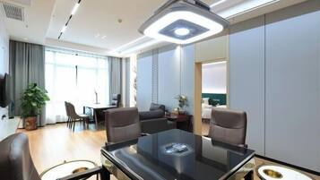 Habitación de hotel moderna con una mesa de comedor de cristal, sillas de cuero, un espejo grande y una lámpara adosada al techo.