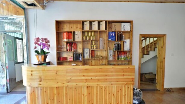 A reception desk with wooden shelving filled with various items, a potted orchid, and a staircase in the background. - Yunshui Jingxiu Inn (Nanjing County)