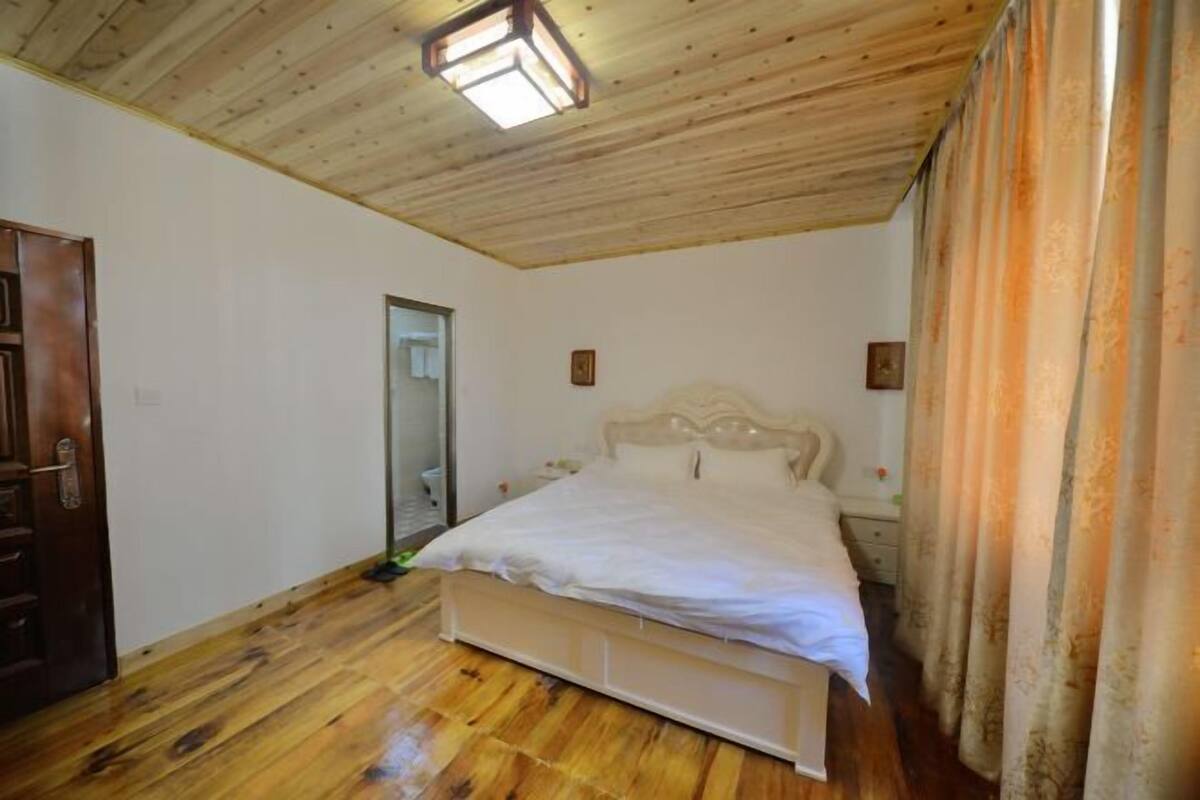 A bedroom with a wooden ceiling, a bed with white bedding, a nightstand, and a mirror on the wall.