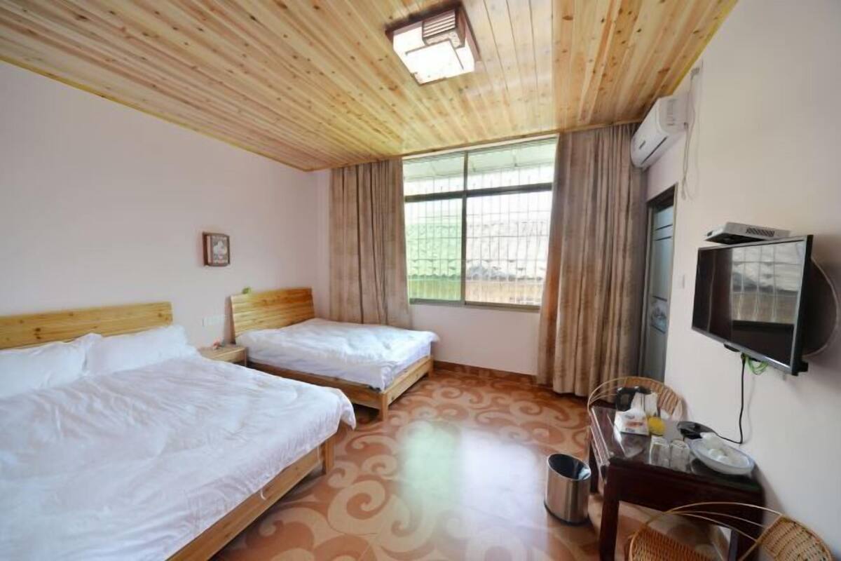 A hotel room with two beds, a television, a desk with a chair, and a window with curtains.