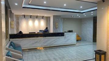 A modern hotel lobby with a marble reception desk, seating area, and a large mirror.