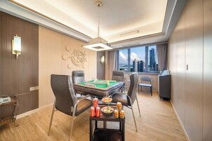 Quarto de hotel com mesa de bilhar, mesa de jantar e cadeiras. Vista da cidade pela janela.
