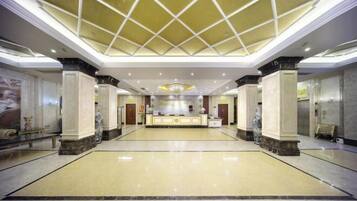 A spacious lobby with a high ceiling, marble flooring, and a reception desk.