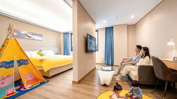 Habitación de hotel con cama, televisor, zona de estar y espacio de juegos para niños.