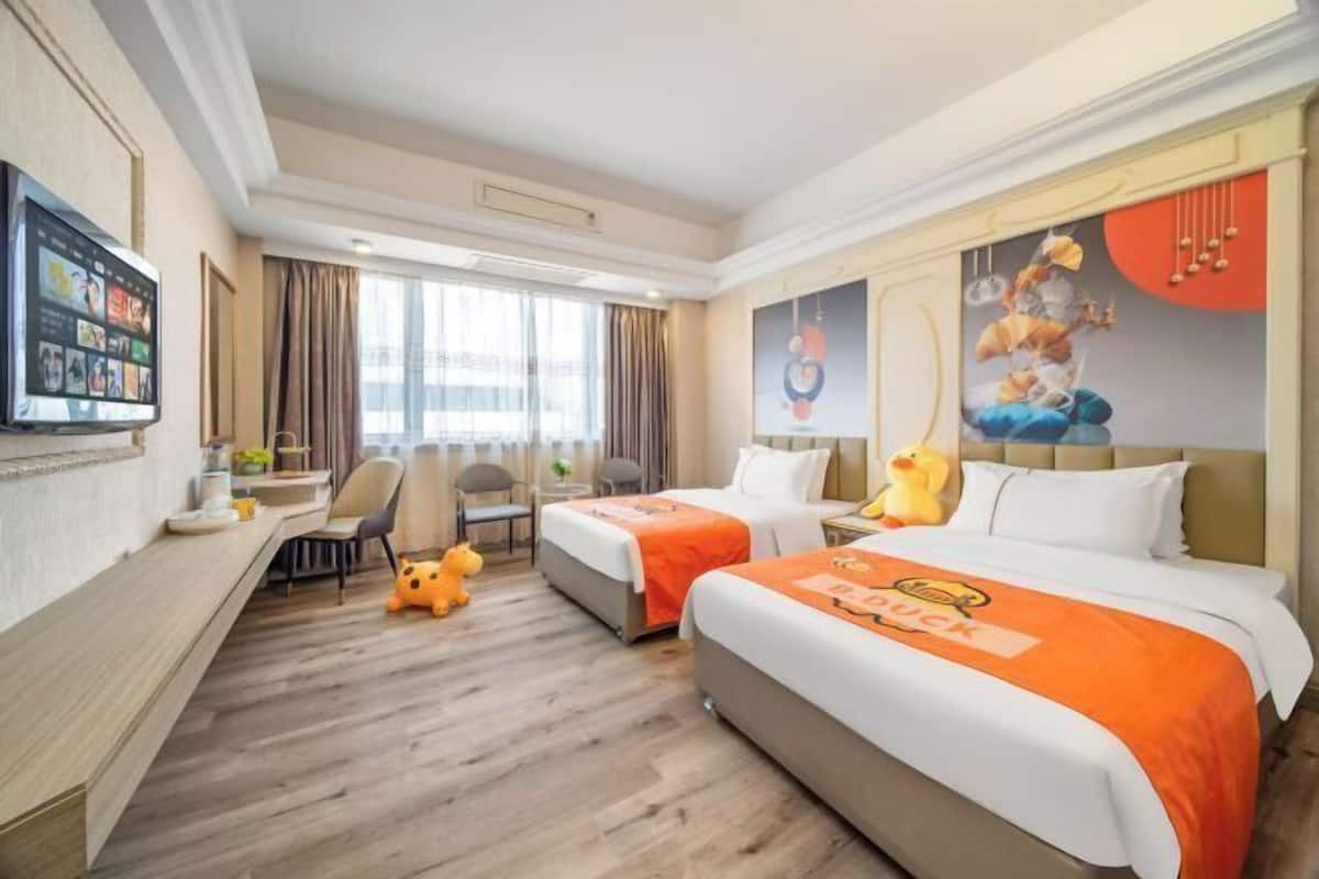 A hotel room with two beds, a desk, a chair, a TV, and a window with curtains.