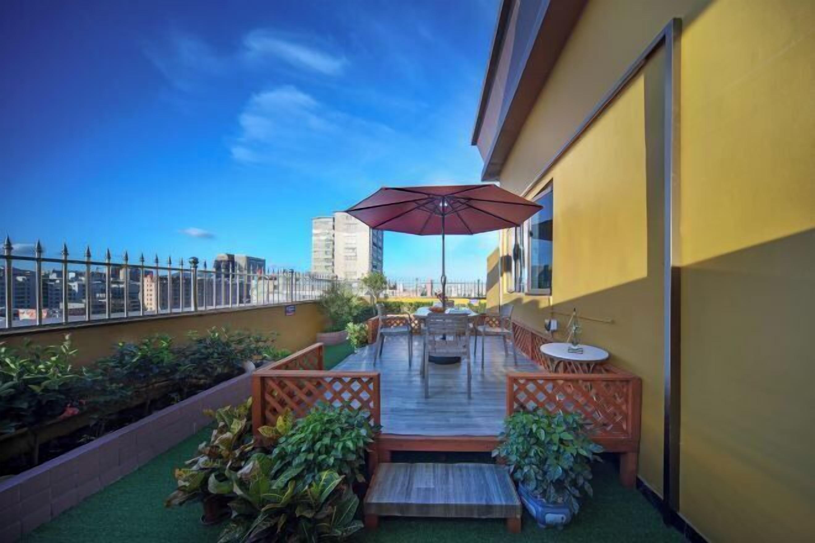 A rooftop terrace with a wooden deck, outdoor seating, and a large umbrella.