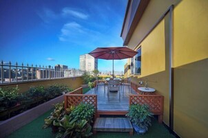 Una terraza en la azotea con piso de madera, asientos al aire libre y un paraguas grande.