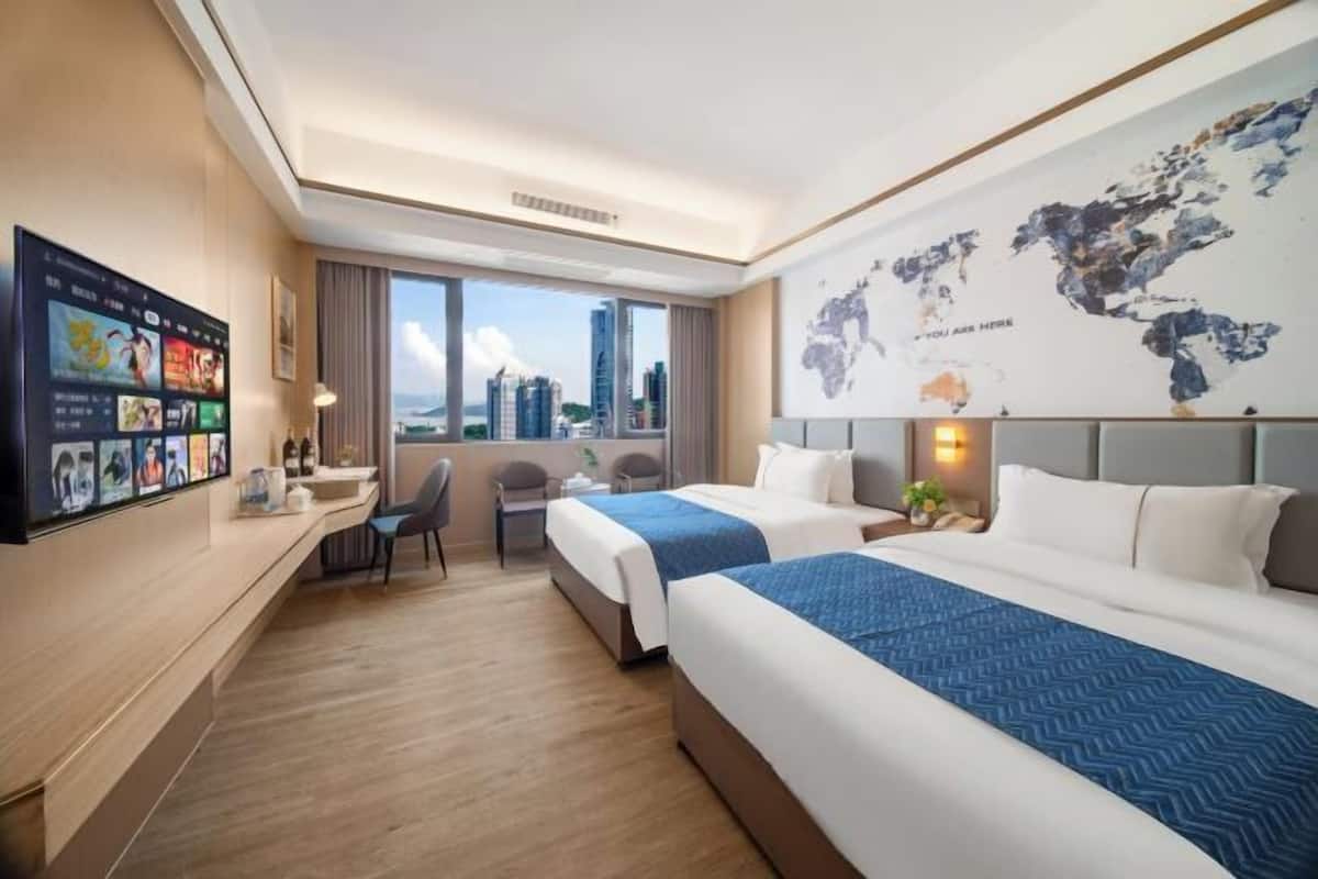 A hotel room with two beds, a desk, a chair, a TV, and a world map on the wall.