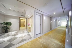 A hotel corridor with a checkered floor pattern, a potted plant, a vase with flowers, and a door leading to another room. - Dongsheng Hotel（Puning International Commodity City · High-speed Rail Station Branch） (Puning)