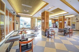 A spacious dining area with checkered flooring, multiple tables and chairs, and a central pillar.