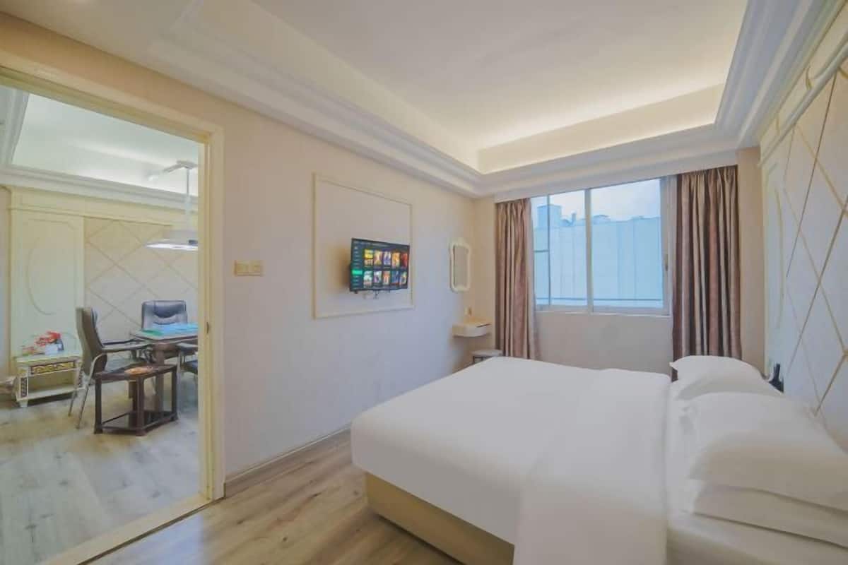 A hotel room with a bed, a desk with a chair, a television, and a window with curtains.