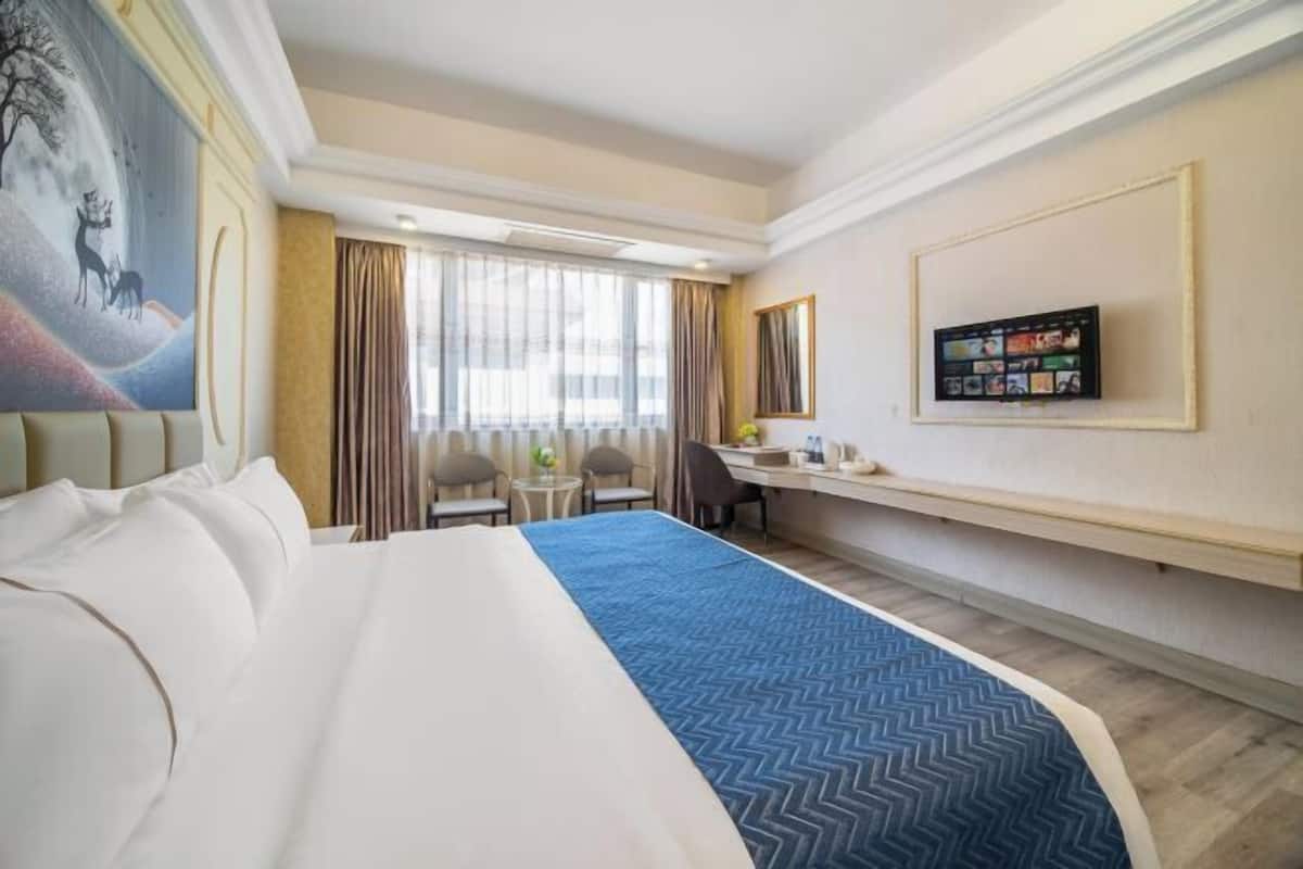 A hotel room with a large bed, a desk, a chair, a television, and a painting on the wall.