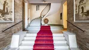 A grand staircase with a red carpet, flanked by brick walls and framed historical paintings. - Domus Consalvi (Ponte Milvio): large design apartment - 3 bedrooms (Roma)