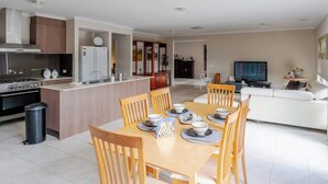 A modern kitchen with a dining area, a living room with a sofa, and a TV. - Elegant 4BR Villa with 3 Living Rooms in PointCook (Point Cook)