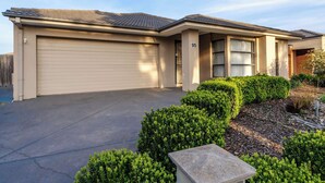 A two-story house with a garage, a number '95' on the side, and a well-maintained front yard with hedges and mulch. - Elegant 4BR Villa with 3 Living Rooms in PointCook (Point Cook)