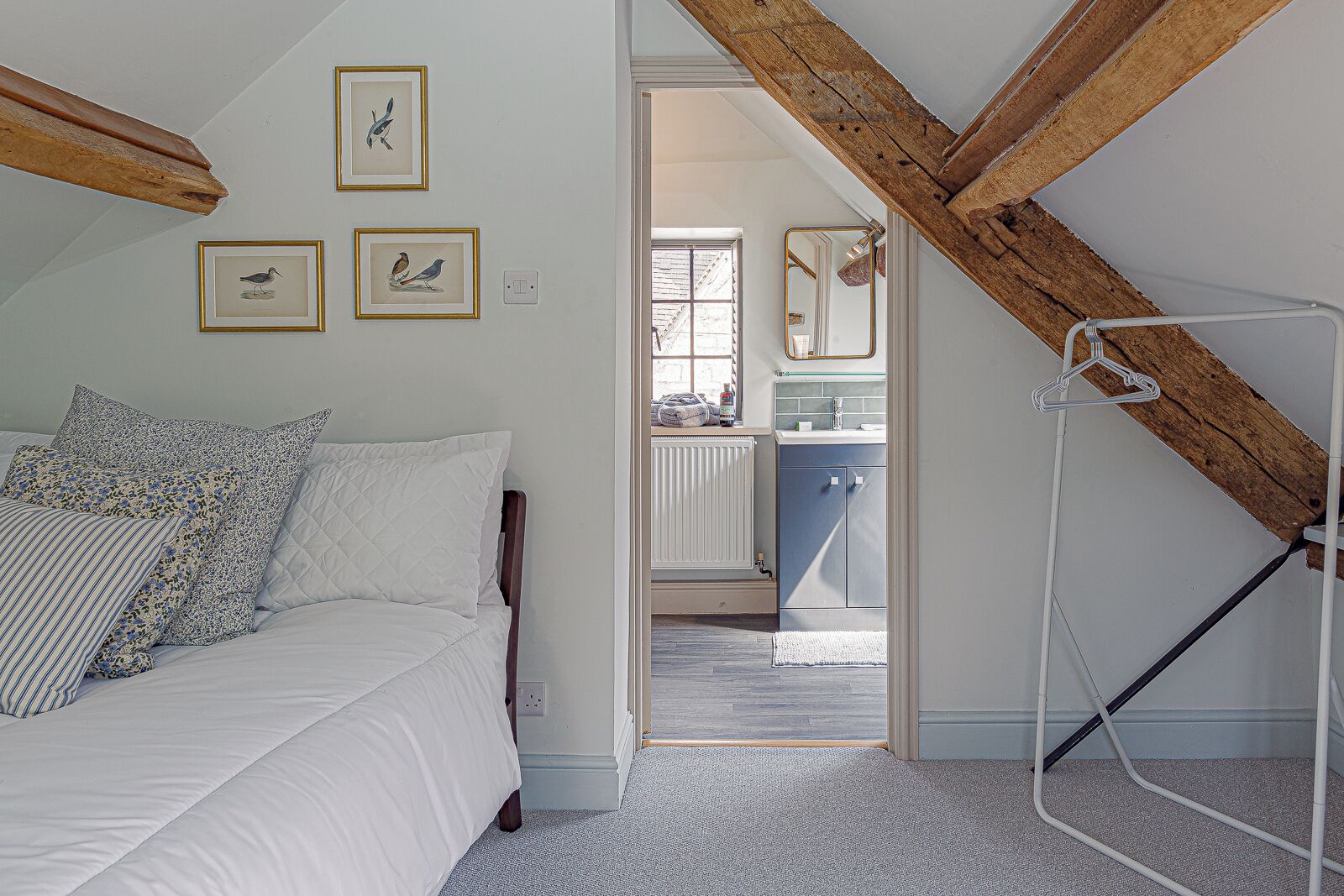 Une chambre à coucher avec un lit, une poutre en bois au plafond et une salle de bain visible à travers une porte ouverte.