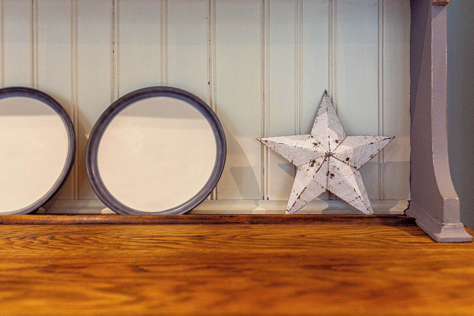 Deux miroirs ronds et une décoration en forme d’étoile de style rustique, le tout posé sur un plancher en bois, devant un mur lambrissé.
