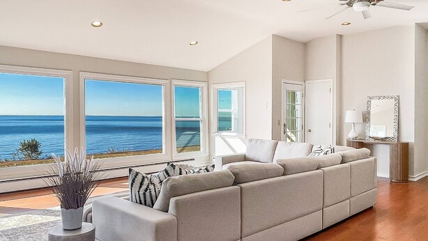 A spacious living room with a large gray sectional sofa, a stone accent piece, and a view of the ocean through large windows. - Akasa Ocean Front Oasis- Seasonal Pool, Grill (Stratford)