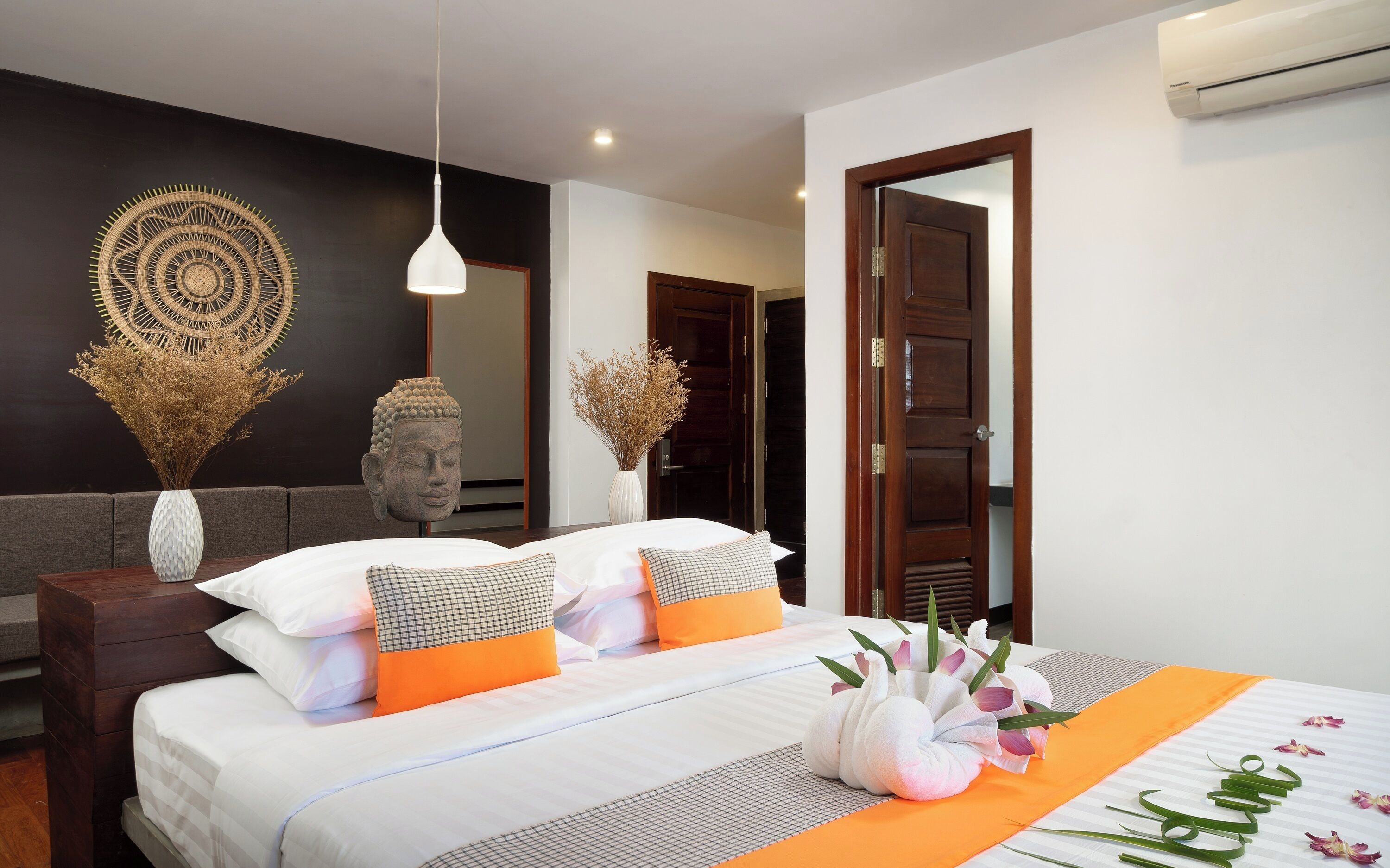 Una habitación de hotel moderna con una cama bien hecha, un espejo grande y una escultura decorativa de Buda.