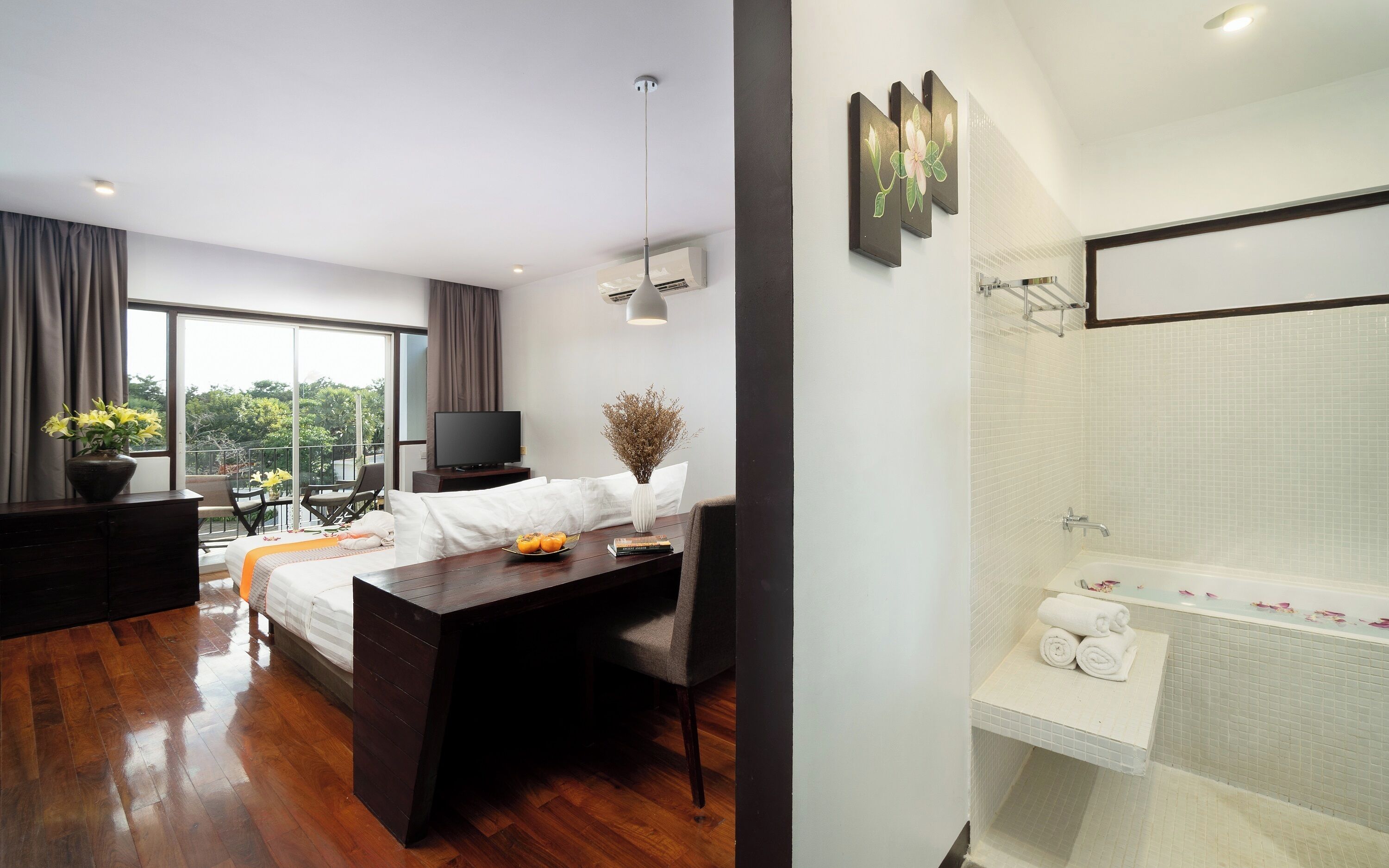 A hotel room with a bed, a desk, a TV, a balcony with a view, and a bathroom with a bathtub and shower.