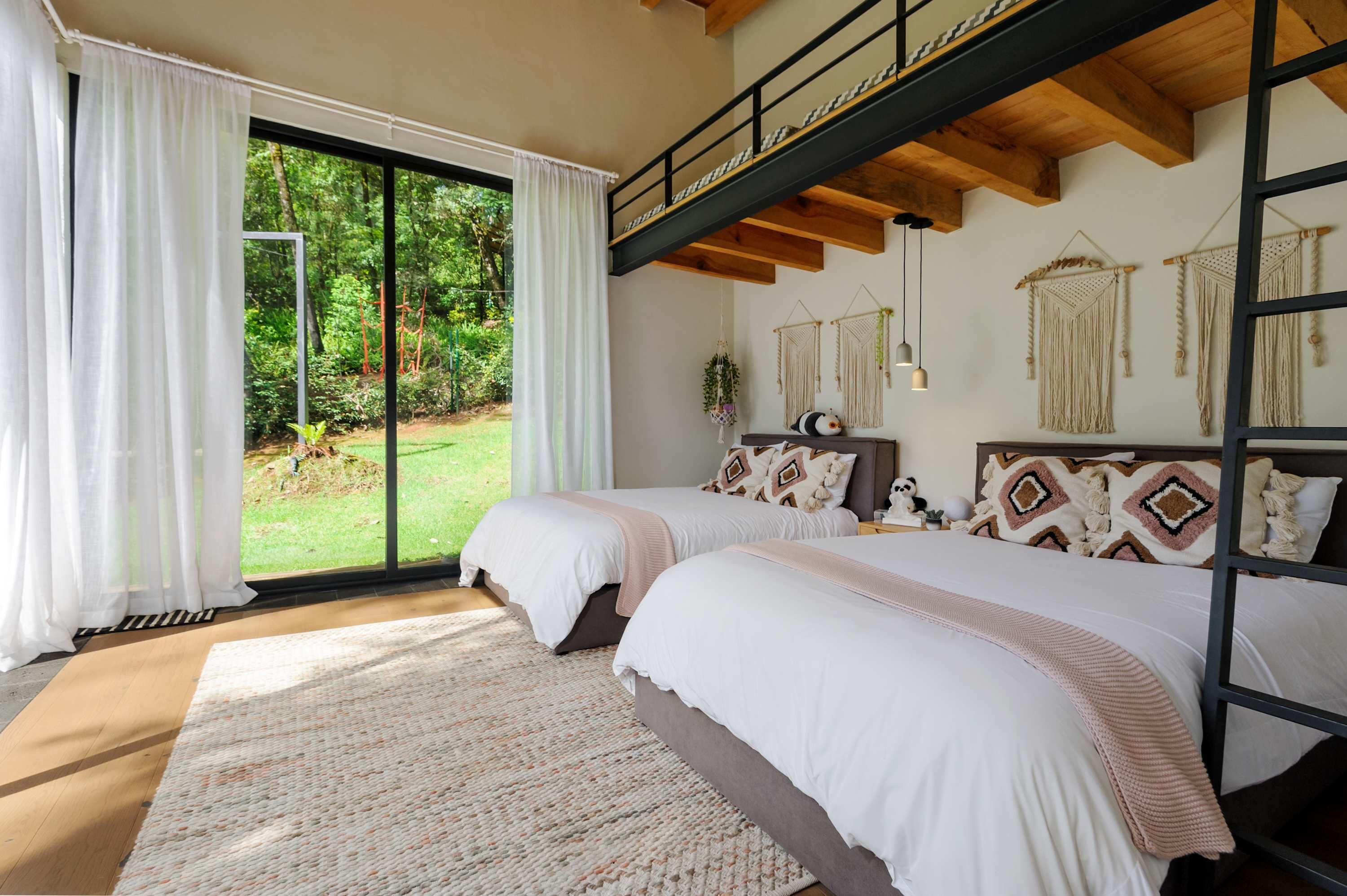 A bedroom with two beds, a large window, and a view of a garden.
