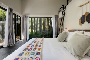 A bedroom with a large bed, a colorful blanket, and a view of greenery through the window.