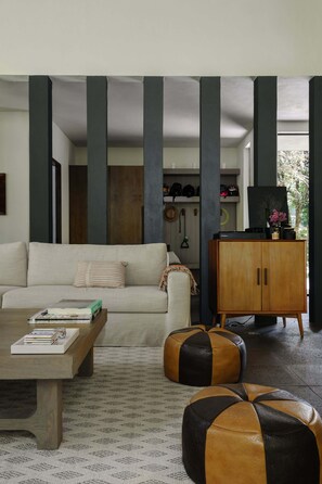 A modern living room with a sofa, coffee table, ottomans, and a wooden cabinet.