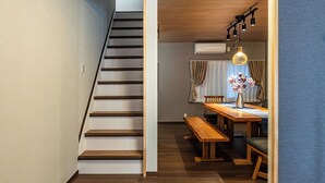 Una escalera conduce a un comedor con una mesa de madera y bancos, una lámpara colgante y un florero con flores.