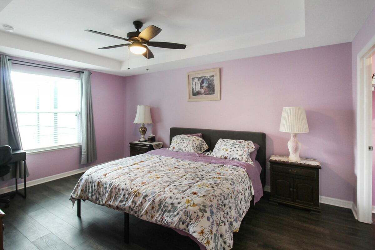 A bedroom with a bed, two bedside tables, a ceiling fan, a window with curtains, and a door.