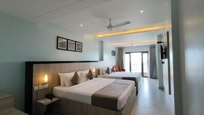 A hotel room with a large bed, bedside tables, a ceiling fan, and a view of the outdoors through a sliding door. - Vbrance - Luxury Boutique Hotel (Puri)