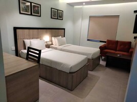 A hotel room with two single beds, a desk, a chair, a red sofa, and a TV.