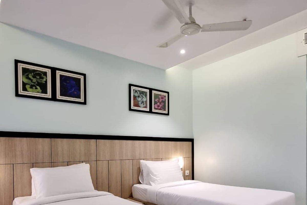 A hotel room with two beds, a ceiling fan, and two framed floral pictures on the wall.