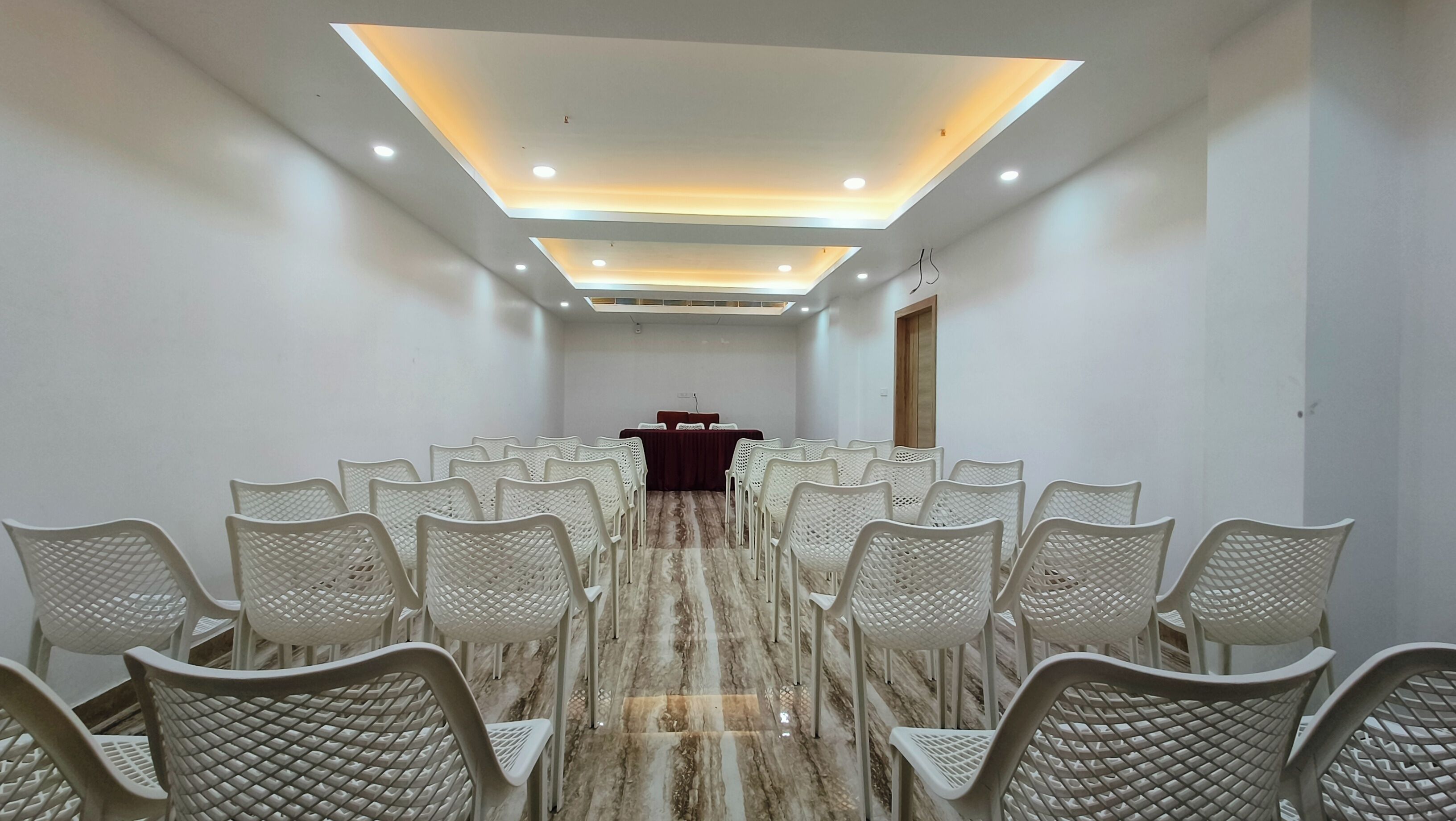 A conference room with white chairs arranged in rows, a podium at the front, and recessed ceiling lighting.
