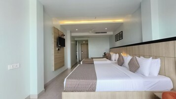 A hotel room with two beds, a TV mounted on the wall, a ceiling fan, and a door leading to another room.