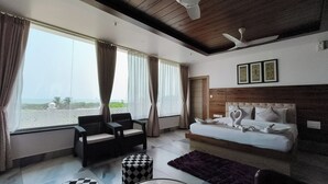 A hotel room with a bed, two chairs, a small table, a purple rug, and a view of the sea. - Vbrance - Luxury Boutique Hotel (Puri)