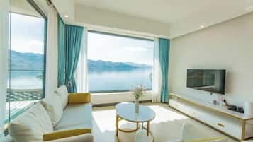 A modern living room with a large TV, comfortable seating, a small round table, and a view of a body of water.
