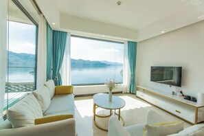 A modern living room with a large TV, comfortable seating, a small round table, and a view of a body of water. - Shuanglang Ziyan Zhuangyuan Inn (Dali City)