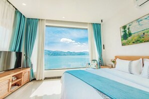 A bedroom with a large bed, a TV on a wooden stand, and a window with a view of the sea. - Shuanglang Ziyan Zhuangyuan Inn (Dali City)