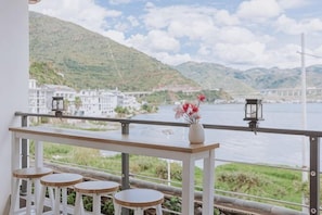 Un balcón con vista a un río, edificios blancos y una montaña.